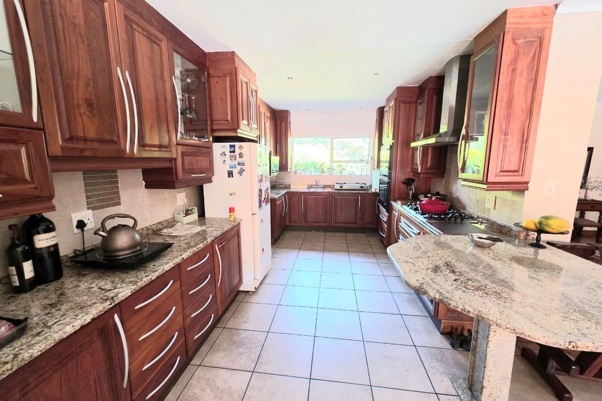 A spacious kitchen featuring wooden cabinetry, granite countertops, a gas hob with extractor fan, and tiled flooring, offering ample workspace and storage.
