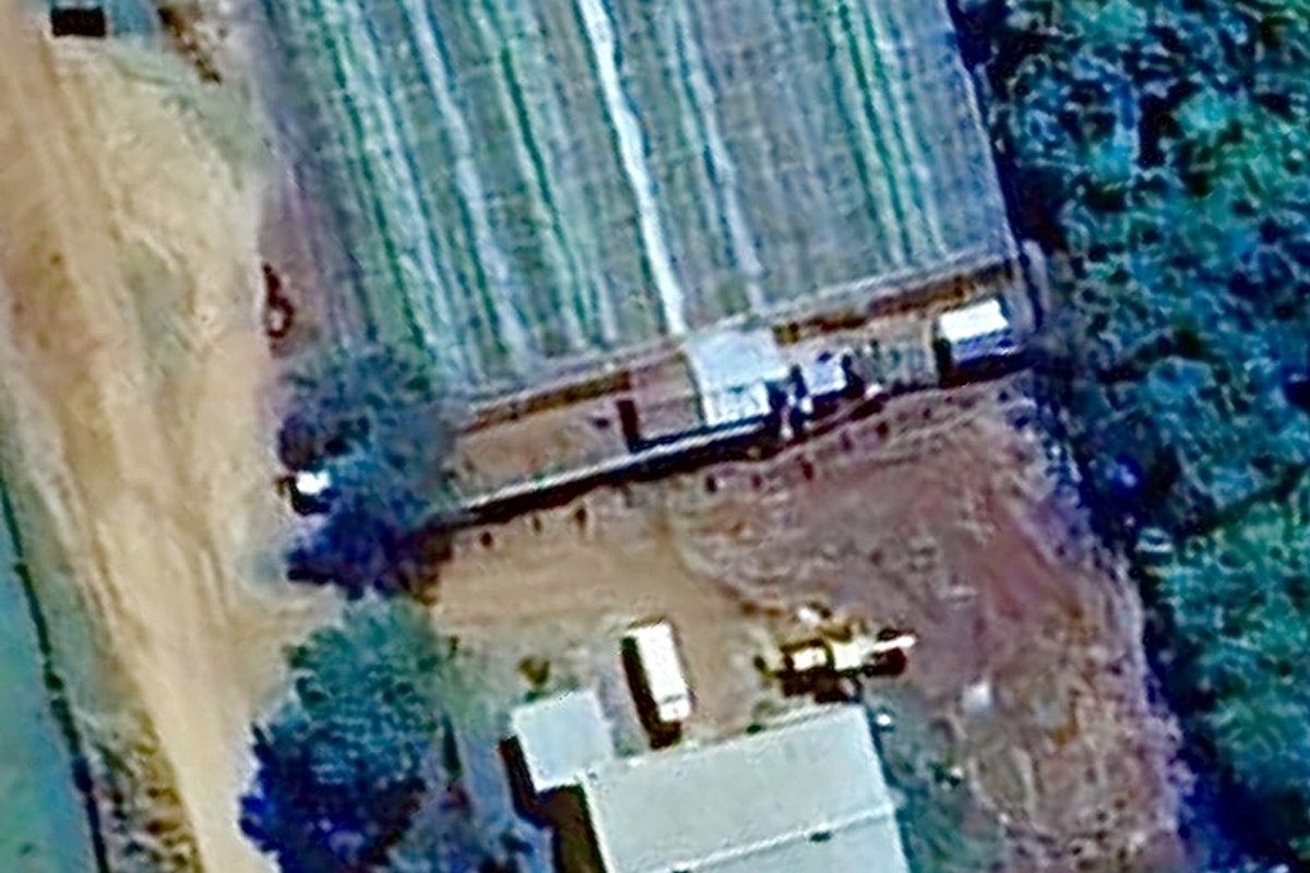 Aerial view of a business property featuring a main building, adjacent greenhouse structures, and surrounding unpaved grounds.
