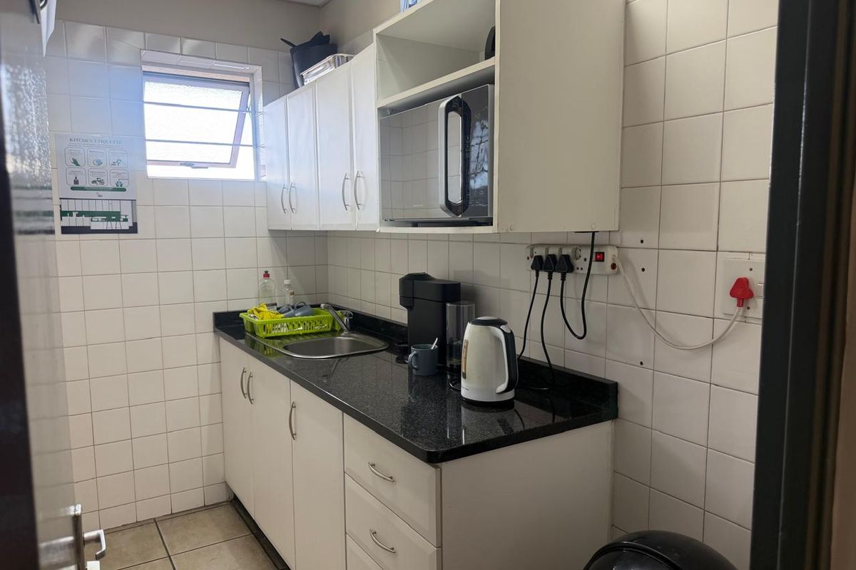Compact kitchenette featuring white cabinetry, dark granite countertops, stainless steel sink, and tiled walls, suitable for office or utility use.