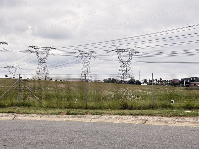 Vacant commercial land featuring perimeter fencing and prominent high-voltage transmission towers, with direct access from a paved street.