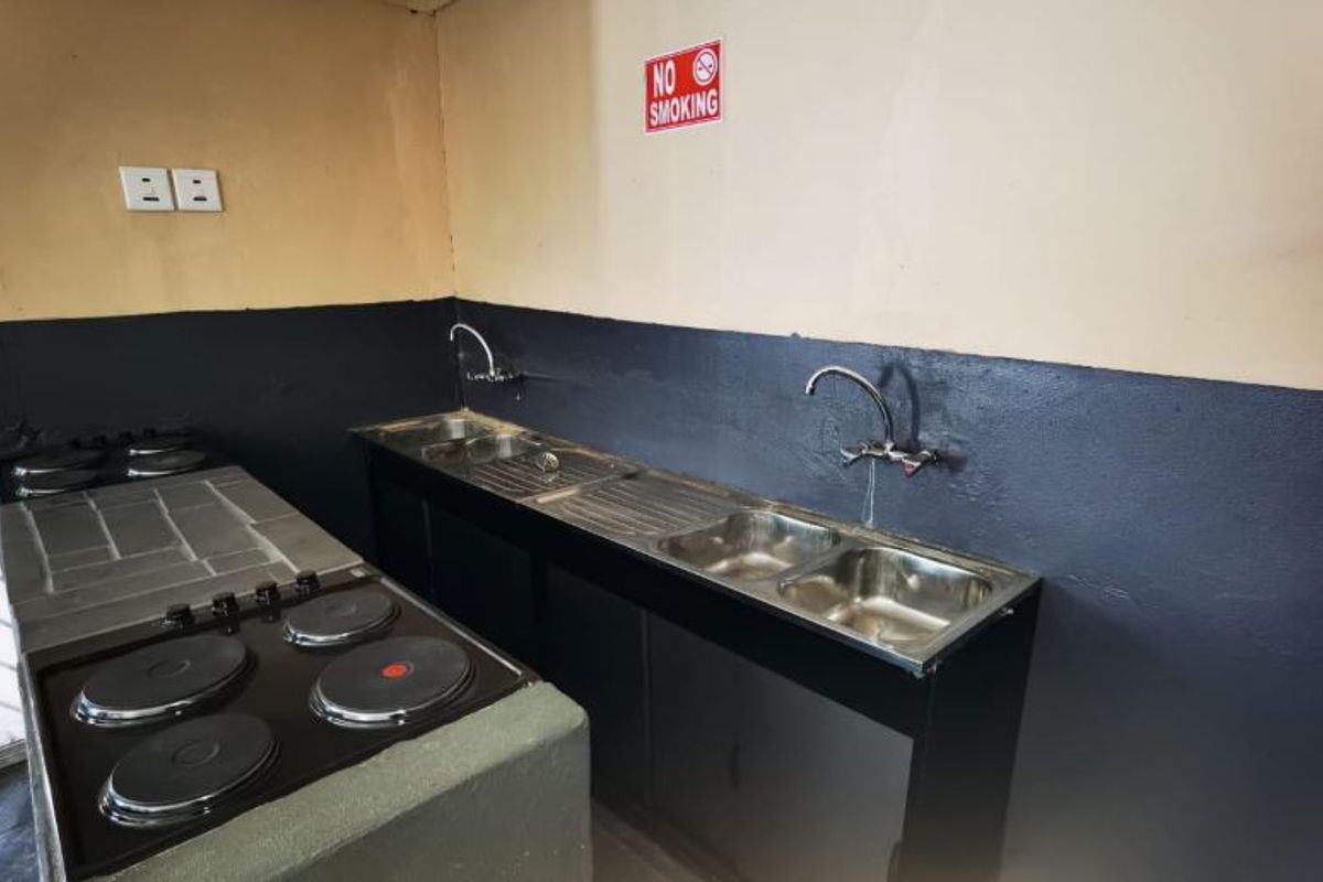 A functional commercial kitchen area featuring a built-in electric hob, stainless steel double sink, and basic cabinetry with a two-tone painted wall finish.