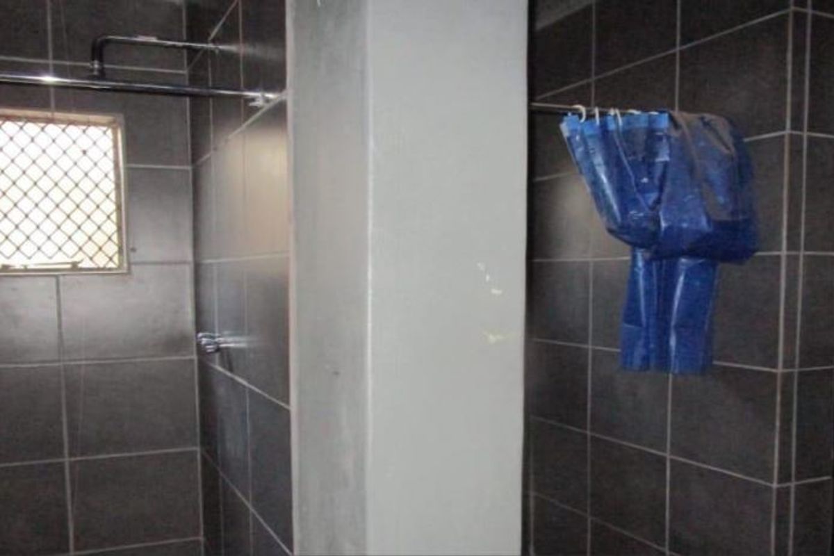 A functional bathroom space featuring dark wall tiling, shower fixtures, and a security window grille, currently in need of cosmetic updates.
