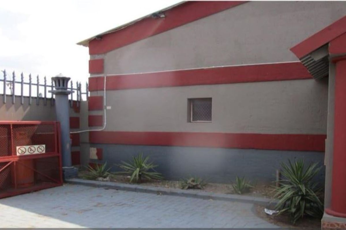 Rear exterior area featuring a paved courtyard, security fencing, and a dedicated gas cylinder storage cage against the building facade.