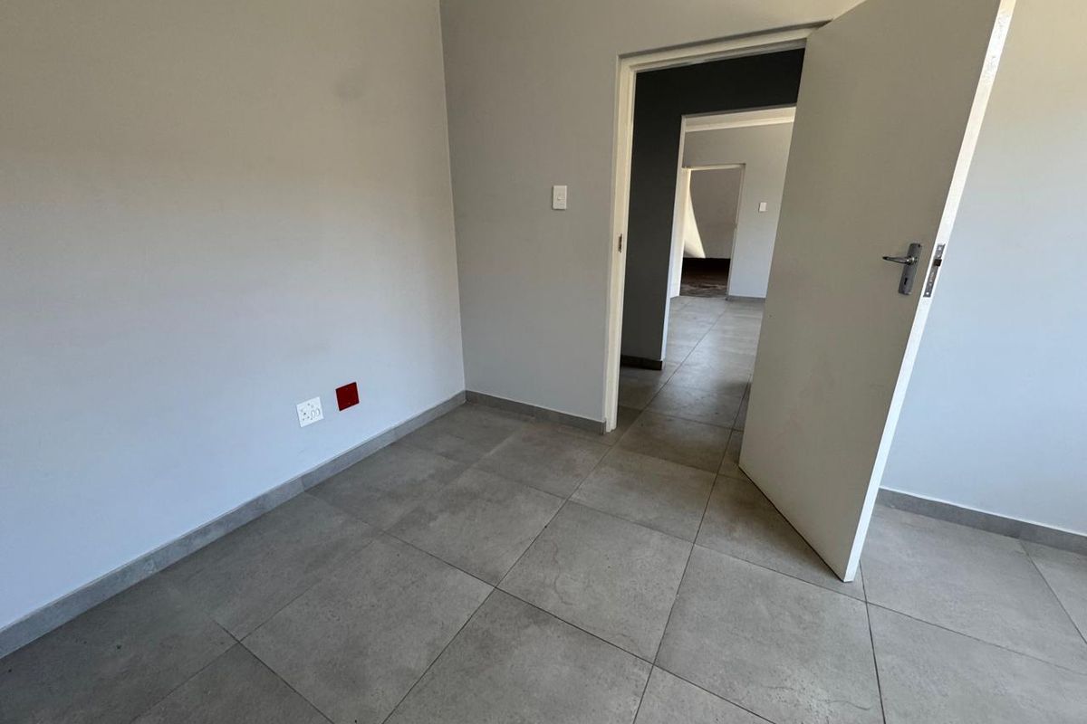 A clean, empty room featuring neutral grey walls, large format floor tiles, and a doorway leading to an adjacent space.
