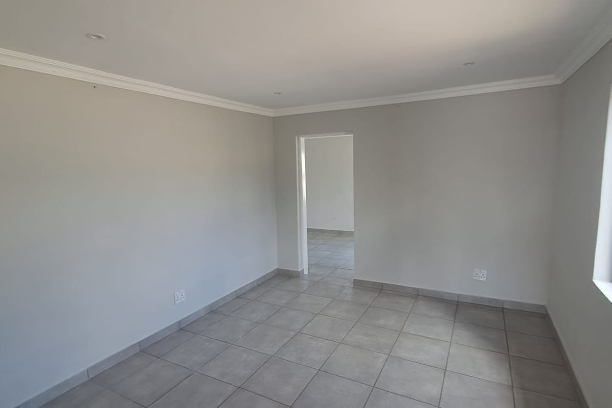 A clean, empty room featuring neutral wall paint, tiled flooring, recessed ceiling lighting, and a doorway leading to an adjacent space.