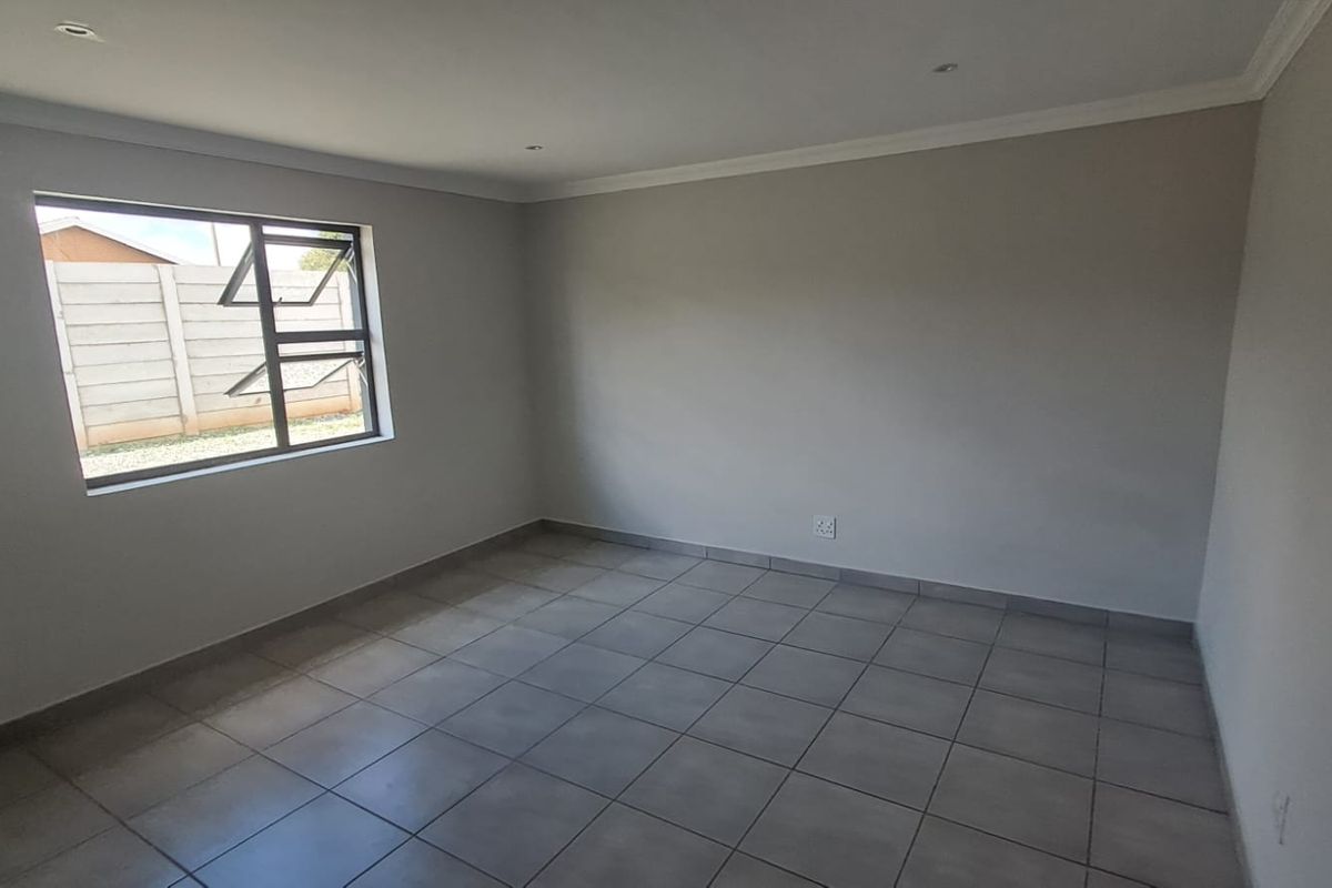A clean, empty room featuring neutral grey floor tiles, smooth painted walls, and a modern aluminium-framed window.