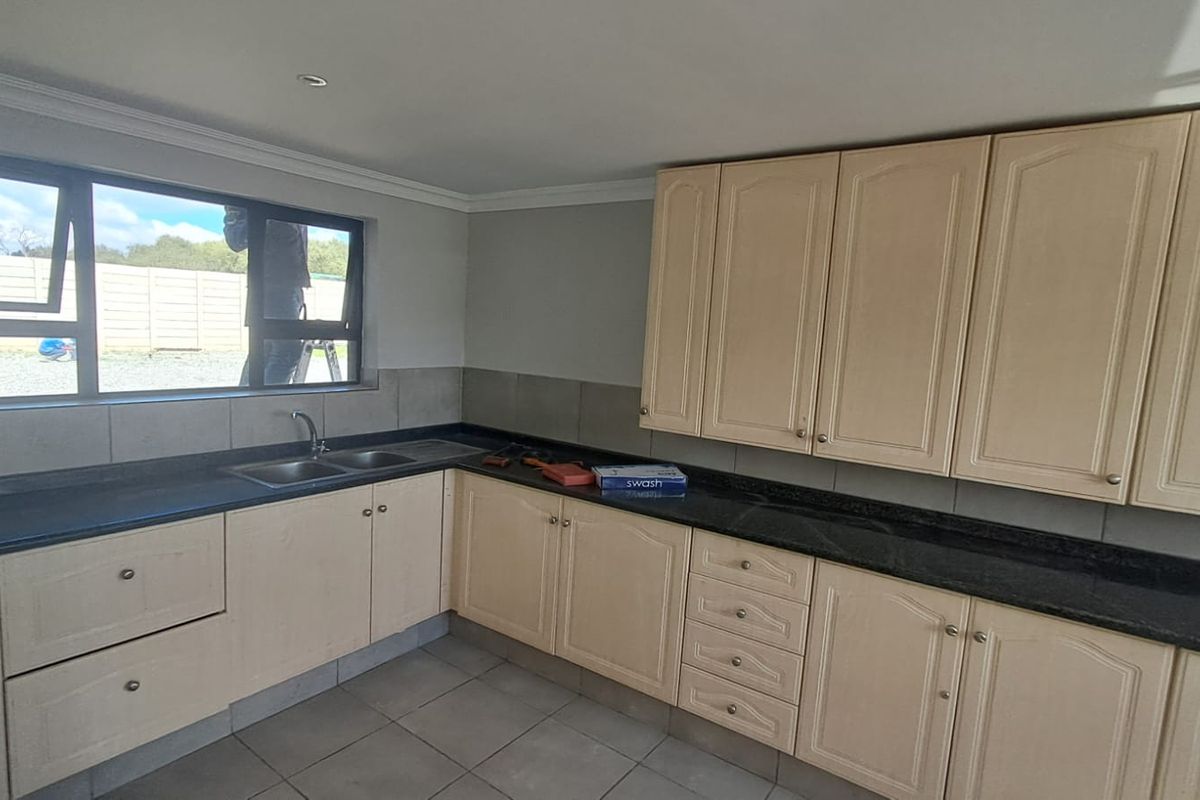 A functional kitchen featuring light-toned cabinetry, dark granite countertops, a double basin sink, and tiled flooring with ample natural light.