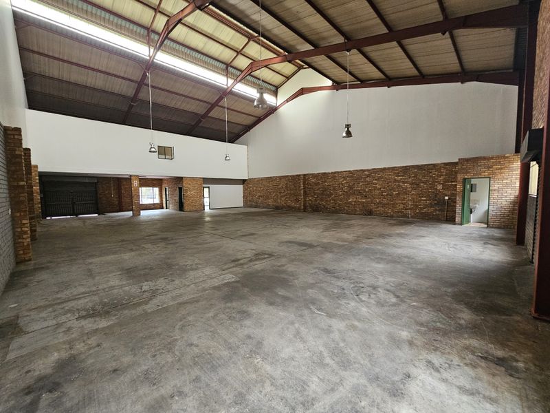 Spacious industrial warehouse unit featuring high ceilings with exposed steel trusses, concrete flooring, and ample natural light through skylights.