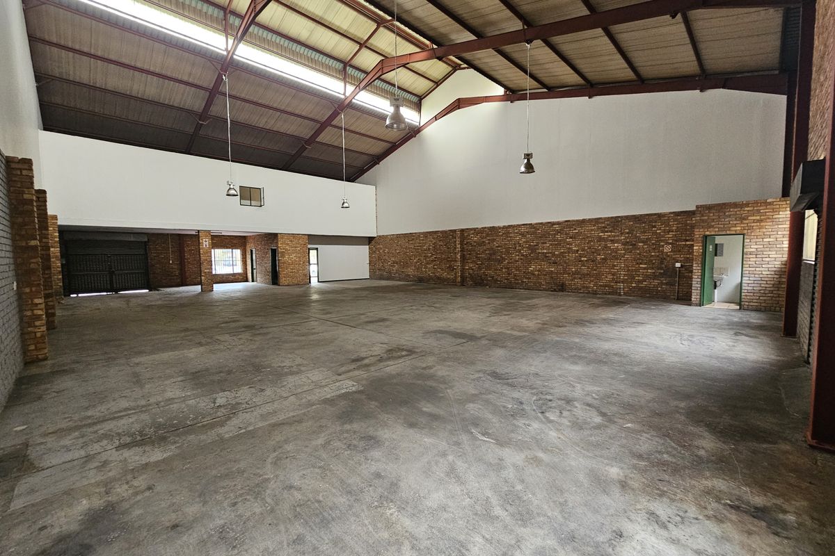 Spacious industrial warehouse unit featuring high ceilings with exposed steel trusses, concrete flooring, and ample natural light through skylights.