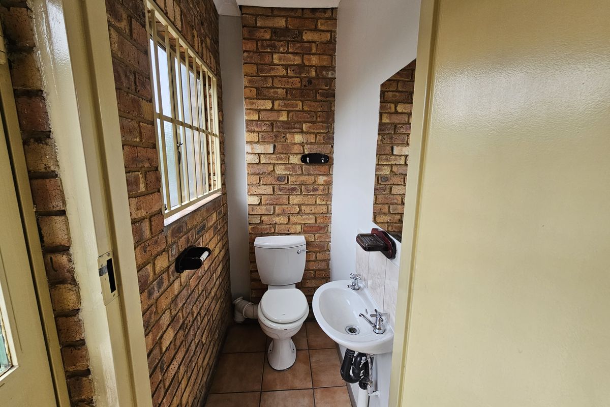Compact bathroom featuring exposed brick walls, ceramic floor tiles, a pedestal basin, and a standard toilet.
