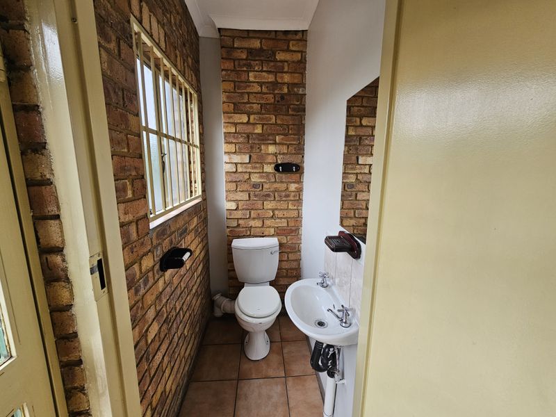 Compact bathroom featuring exposed brick walls, ceramic floor tiles, a pedestal basin, and a standard toilet.