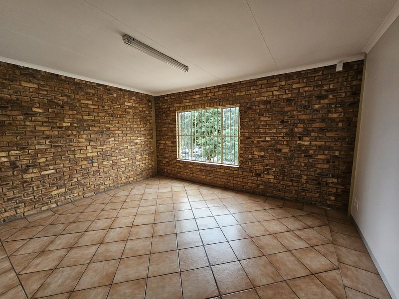 An empty office space featuring exposed brick walls, ceramic tile flooring, and a window fitted with security bars.