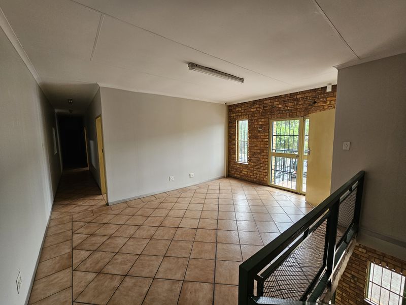 An empty industrial-style landing area featuring exposed brickwork, ceramic tile flooring, and a metal security gate leading to an exterior balcony.