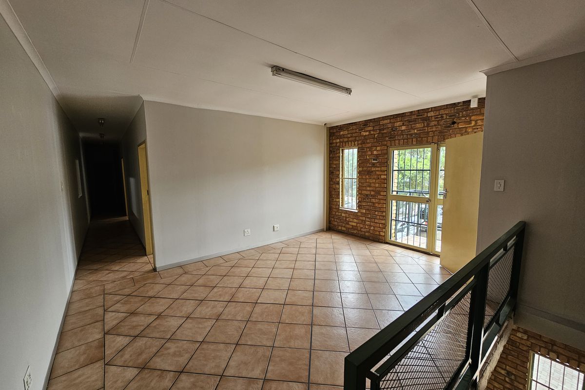 An empty industrial-style landing area featuring exposed brickwork, ceramic tile flooring, and a metal security gate leading to an exterior balcony.