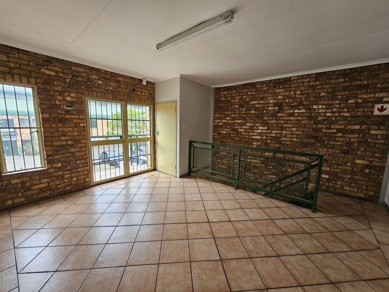 Spacious industrial-style hallway featuring exposed brick walls, ceramic tiled flooring, and a metal staircase railing, providing a functional and open transition area.