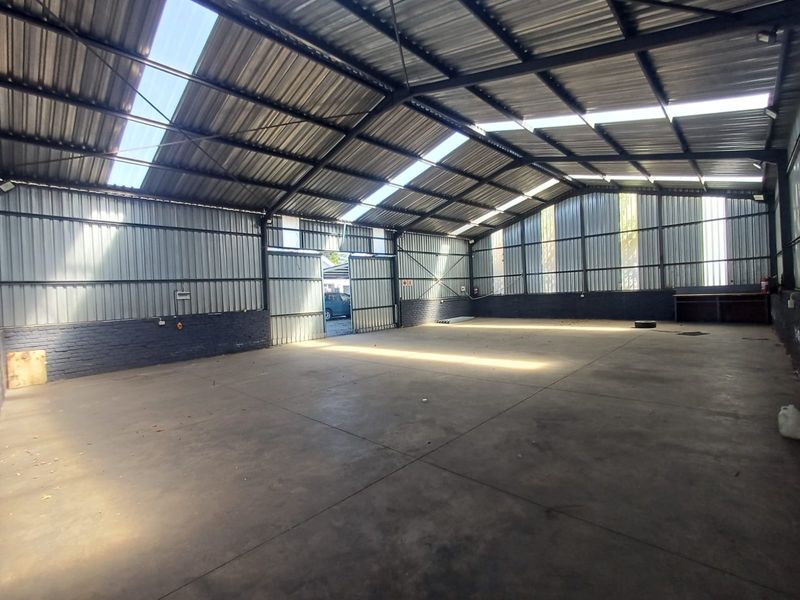 Spacious industrial warehouse unit featuring high ceilings with integrated skylights, concrete flooring, and large sliding access doors, suitable for storage or workshop use.
