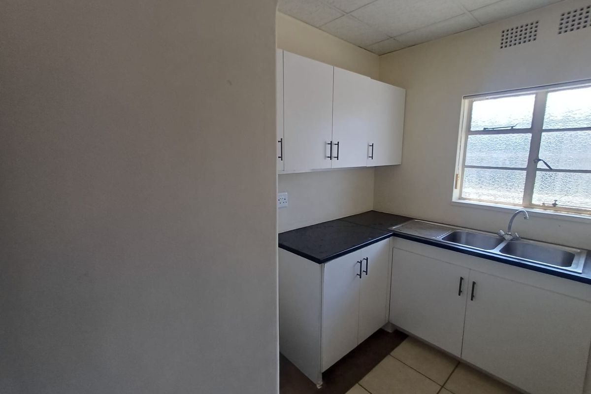 A functional kitchen area featuring white built-in cabinetry, dark laminate countertops, a stainless steel double sink, and tiled flooring.