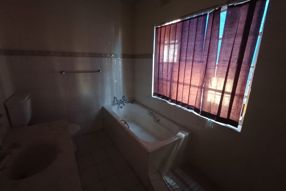 A functional bathroom featuring a built-in bathtub, tiled walls, and a vanity basin, offering a blank canvas for potential modernization.