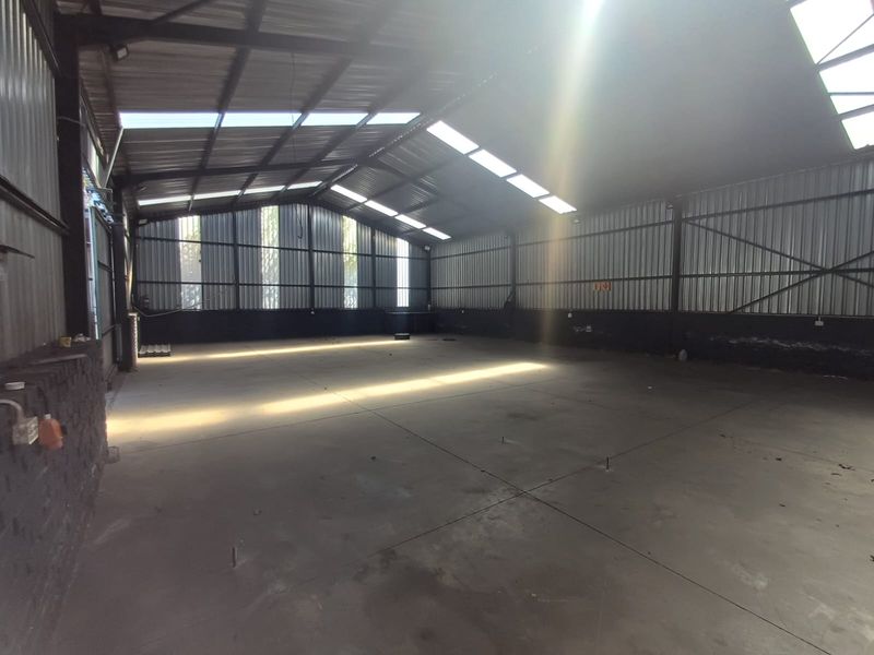 Spacious industrial warehouse unit featuring high ceilings with integrated skylights, corrugated metal walls, and durable concrete flooring, suitable for various commercial or storage uses.