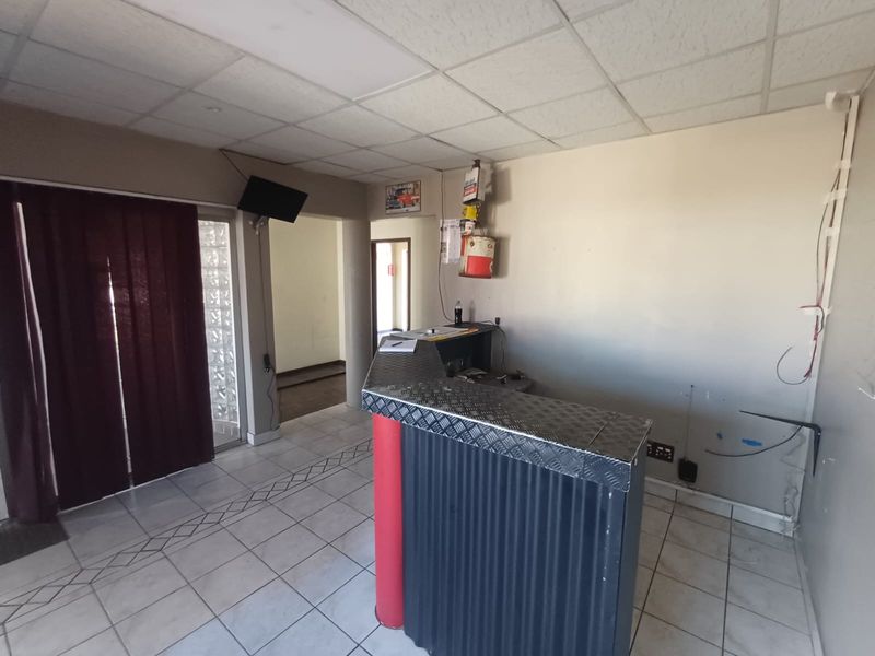 Industrial reception area featuring a custom metal-clad desk, tiled flooring, and suspended ceiling, currently vacant and ready for refurbishment.