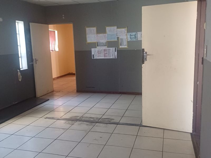 An empty office space featuring ceramic floor tiles and a suspended ceiling, providing a functional layout for industrial or commercial use.