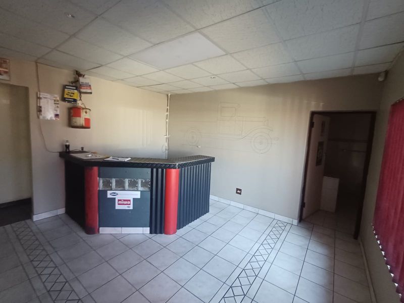 Industrial office space featuring a built-in reception counter, tiled flooring, and a suspended ceiling, suitable for a workshop or service center reception area.