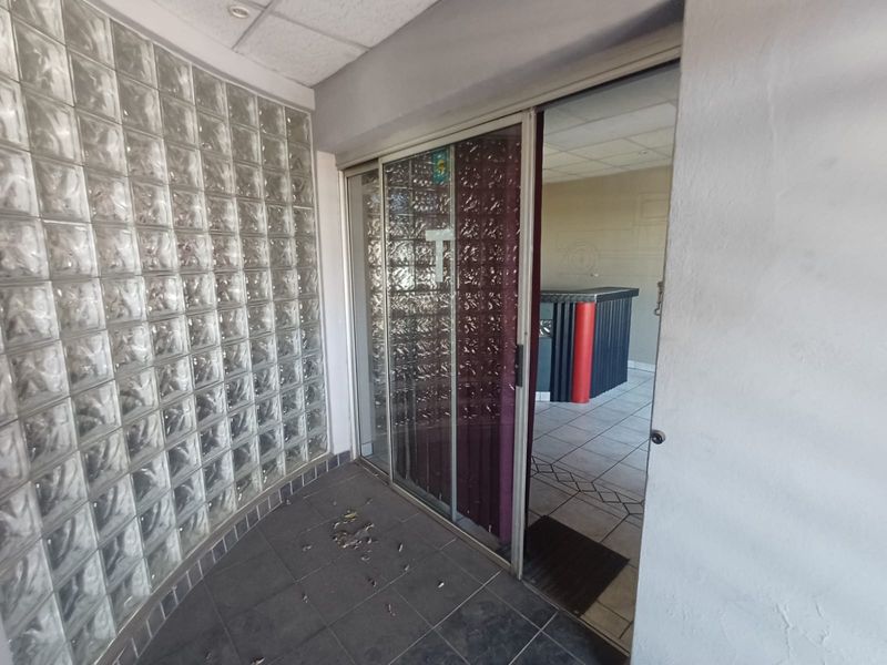 Entrance area featuring a decorative glass block wall, sliding glass door access, and tiled flooring, leading into an open industrial space.