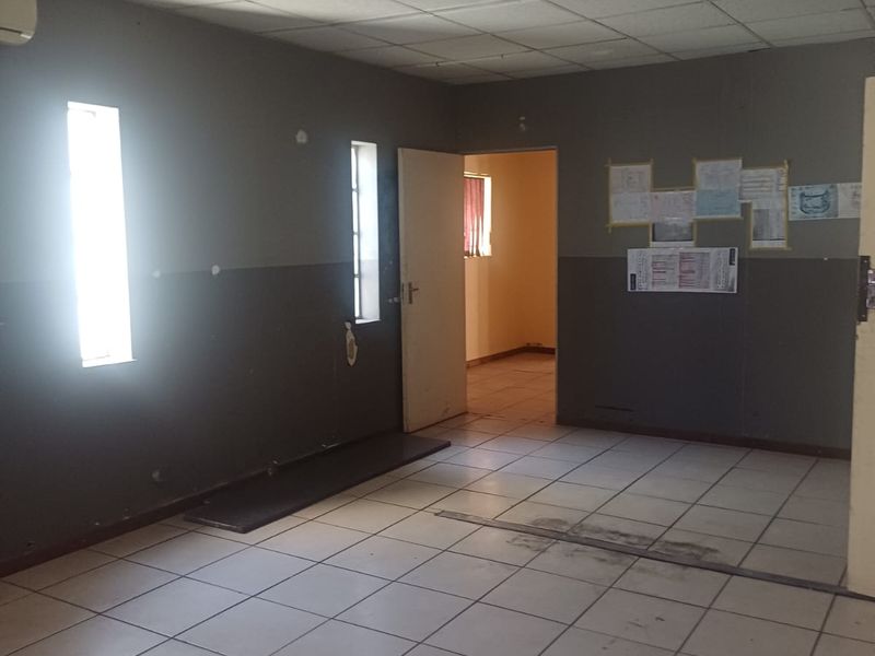 An empty industrial office space featuring ceramic tiled flooring, a suspended ceiling, and an integrated air conditioning unit.