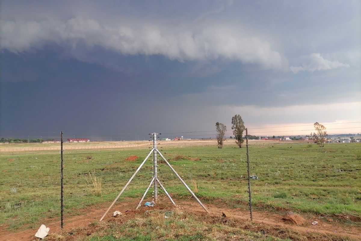 Expansive open land area featuring perimeter electric fencing under a dramatic stormy sky.