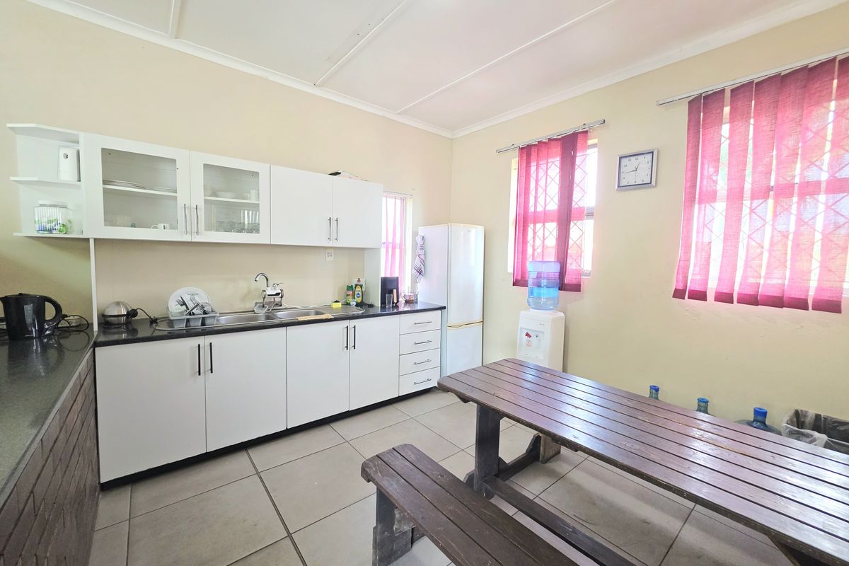 Functional kitchen area featuring white built-in cabinetry, dark countertops, stainless steel sink, and tiled flooring with security bars on the windows.