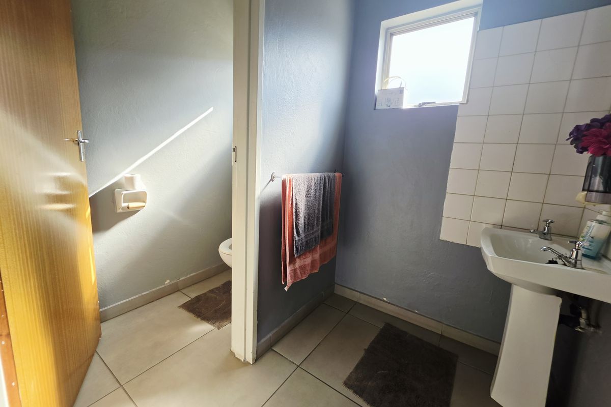 A functional bathroom featuring a pedestal washbasin, tiled splashback, and a separate toilet area with tiled flooring and natural light.
