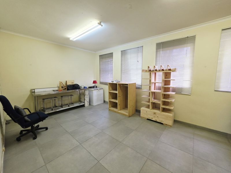 A spacious, functional office or utility room featuring neutral tiled flooring, large windows with venetian blinds, and overhead fluorescent lighting.