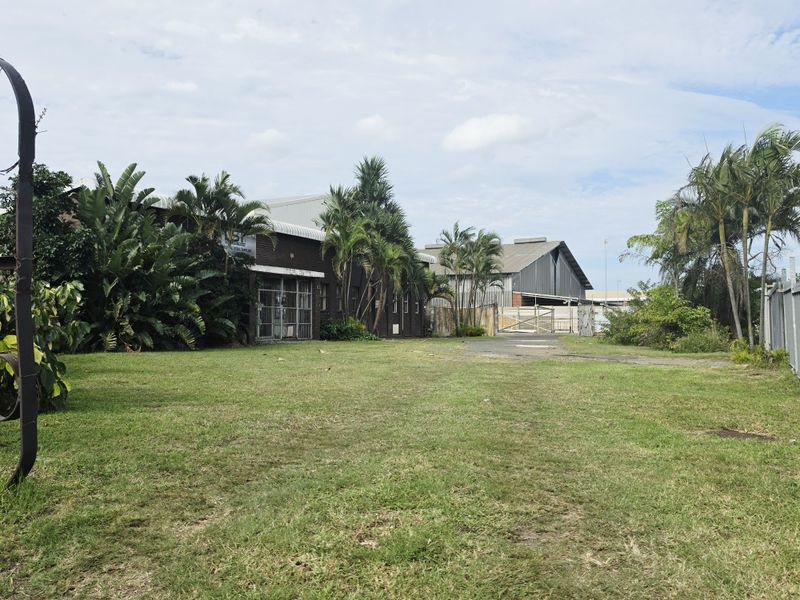 Exterior view of an industrial warehouse property featuring a large grassed area, paved driveway, and secure gated access points.