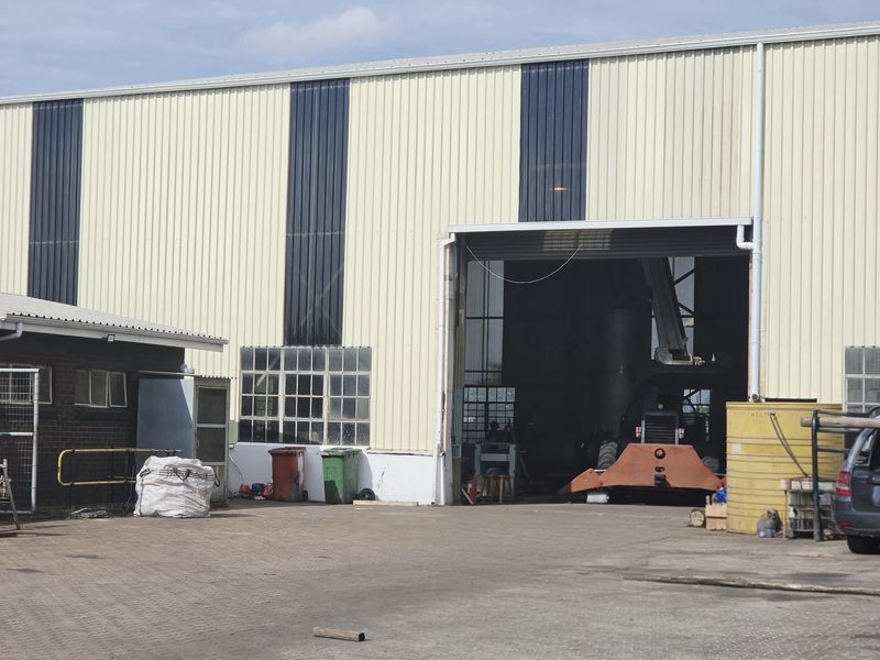 Industrial warehouse facility featuring a large roller shutter door, corrugated metal cladding, and an adjacent brick annex building with a paved yard area.