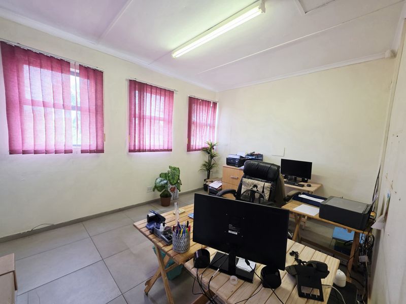 A functional office space featuring tiled flooring, multiple windows with vertical blinds, and overhead fluorescent lighting.