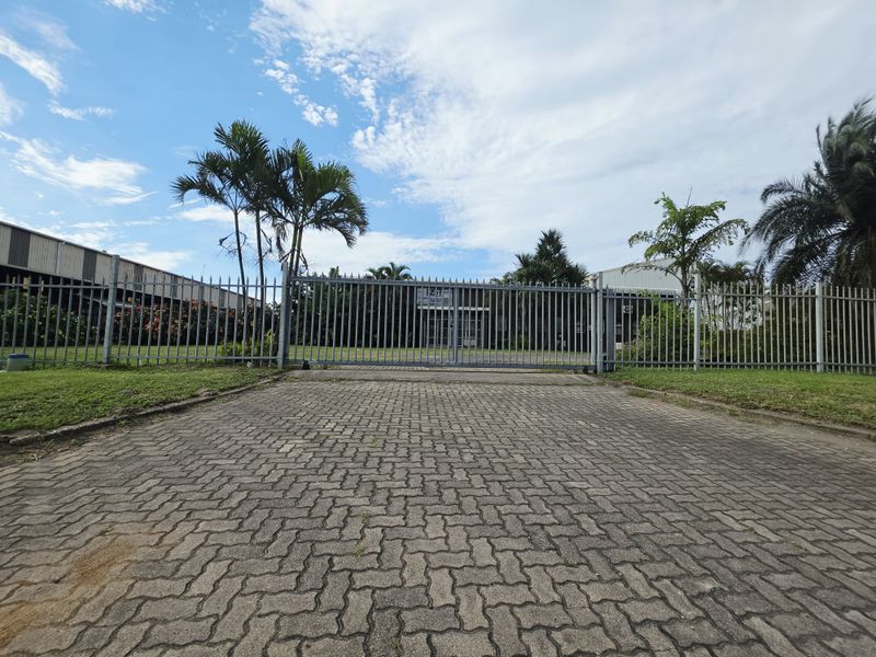 Front view of the property featuring a secure metal gate, paved driveway, and established garden area.