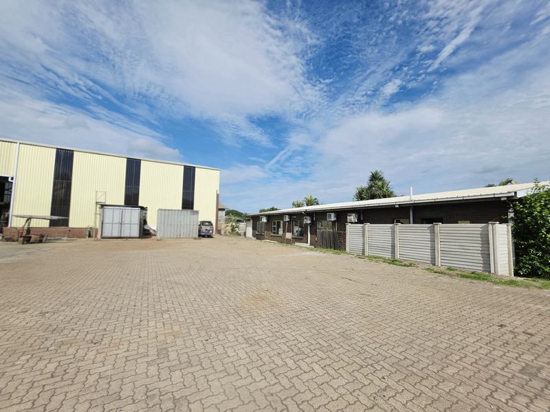 Spacious paved yard area featuring an industrial warehouse structure and a secondary building with wall-mounted air conditioning units.