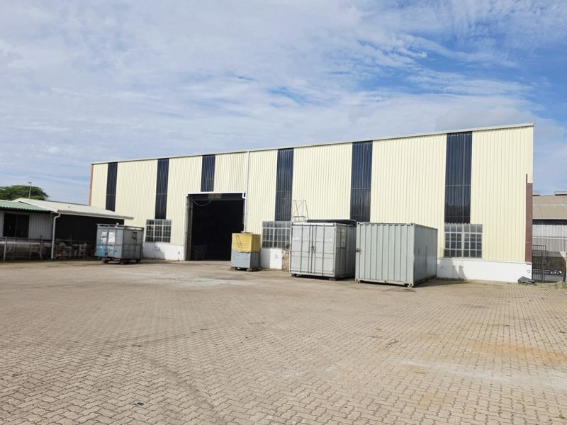 Rear view of an industrial warehouse featuring corrugated metal cladding, a large roller shutter door, and an expansive paved yard area.