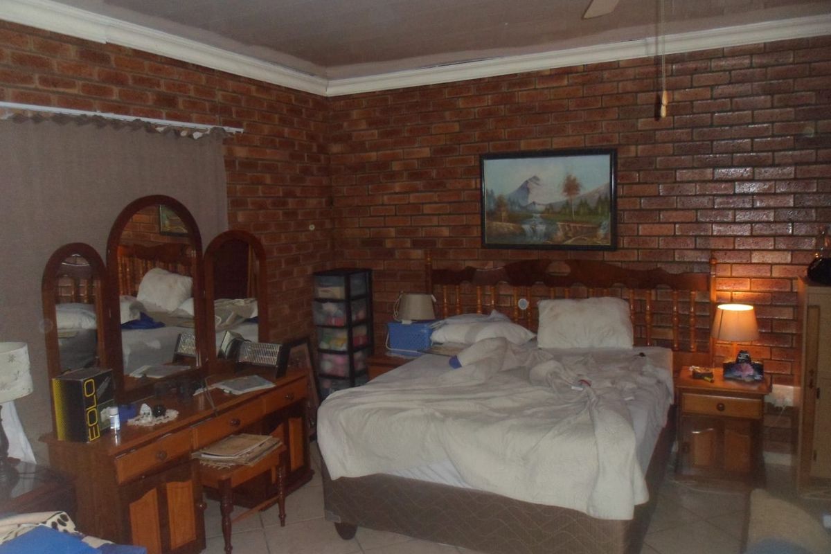 A bedroom featuring exposed brick walls, tiled flooring, and a ceiling fan, offering a rustic aesthetic.