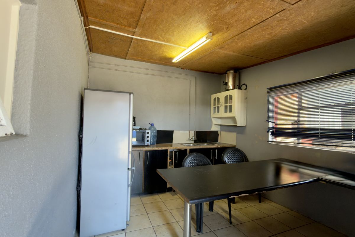 A functional kitchen area featuring basic cabinetry, a sink, tiled flooring, and a window with venetian blinds, requiring cosmetic updates to improve aesthetics.