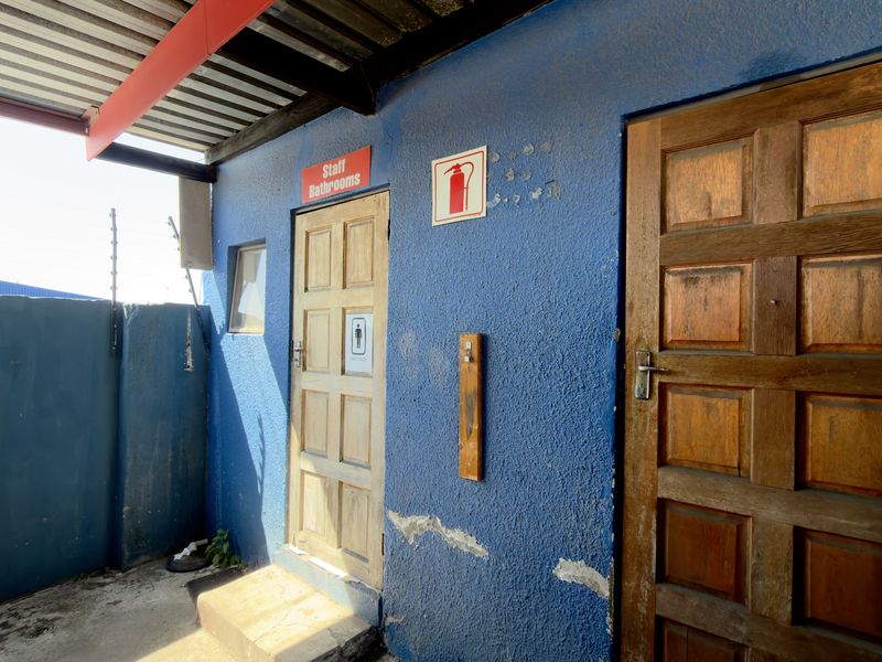 Exterior rear area featuring staff bathroom access, corrugated roofing, and security fencing with visible wear to the painted wall surfaces.