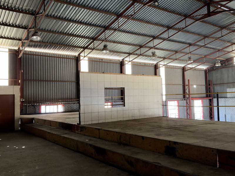 Spacious industrial utility area featuring a raised mezzanine platform, exposed steel roof structure, and a central tiled partition wall.