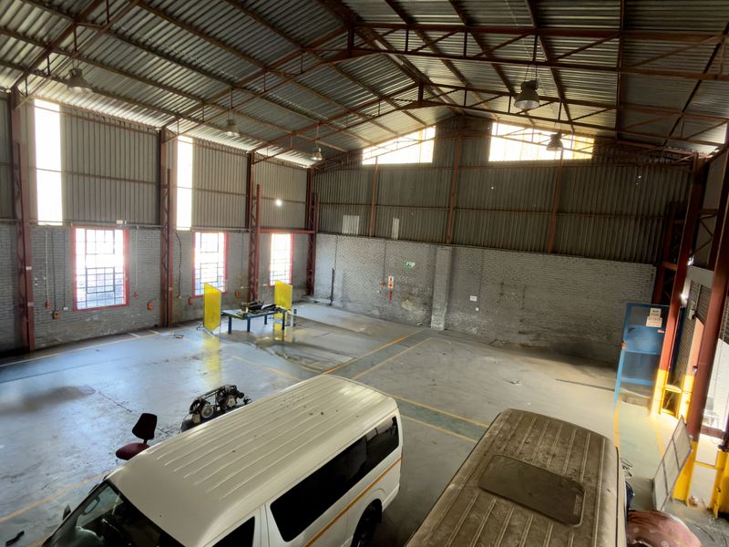 Spacious industrial warehouse unit featuring high ceilings with exposed steel trusses, concrete flooring, and large windows providing ample natural light.