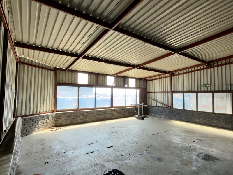 Spacious industrial utility area featuring exposed steel roof trusses, corrugated metal walls, and large windows providing ample natural light.