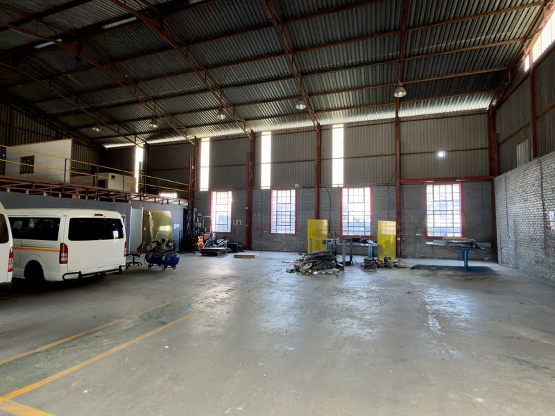 Spacious industrial warehouse featuring high ceilings with exposed steel trusses, concrete flooring, and a mezzanine level, suitable for various commercial or storage applications.