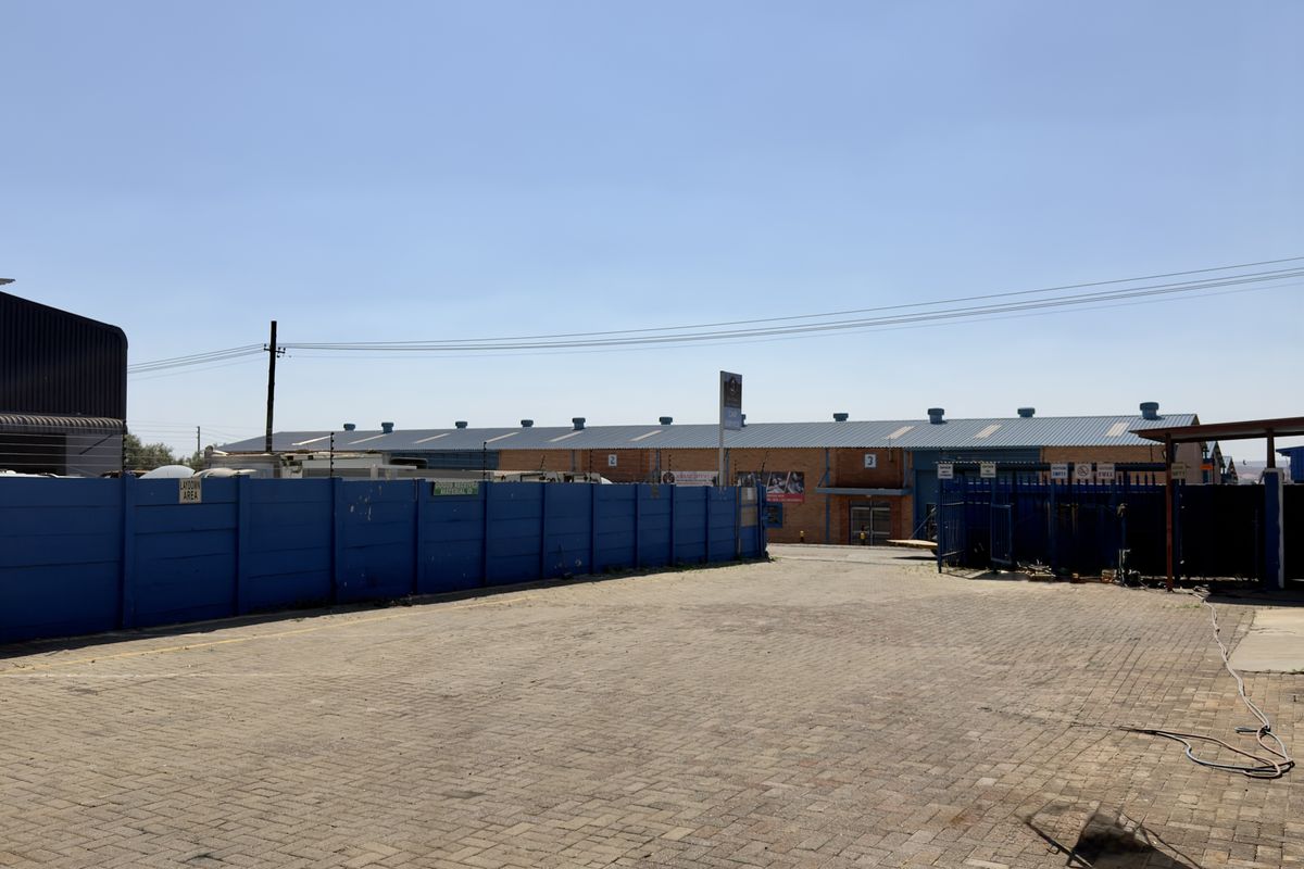 A spacious paved industrial yard area featuring a perimeter wall with electric fencing and access to the main warehouse building.