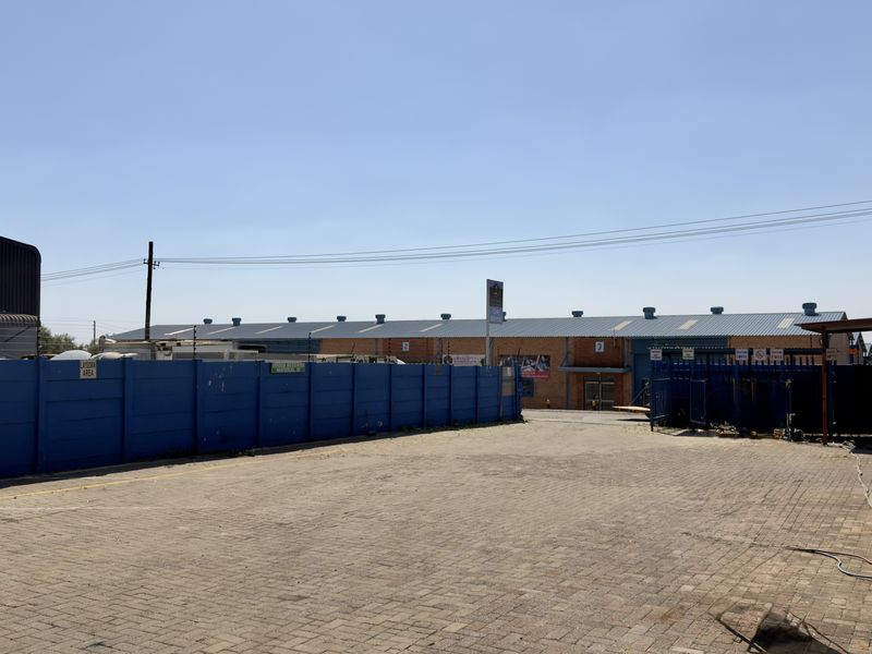 A spacious paved industrial yard area featuring a perimeter wall with electric fencing and access to the main warehouse building.