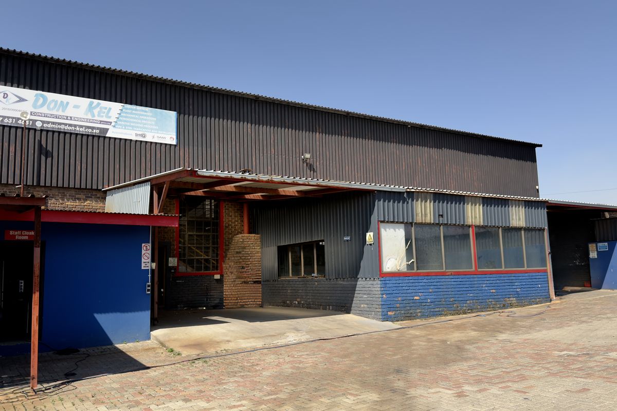 Front elevation of a commercial industrial facility featuring corrugated metal cladding, brick masonry, and a paved driveway entrance.