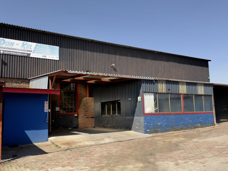 Front elevation of a commercial industrial facility featuring corrugated metal cladding, brick masonry, and a paved driveway entrance.