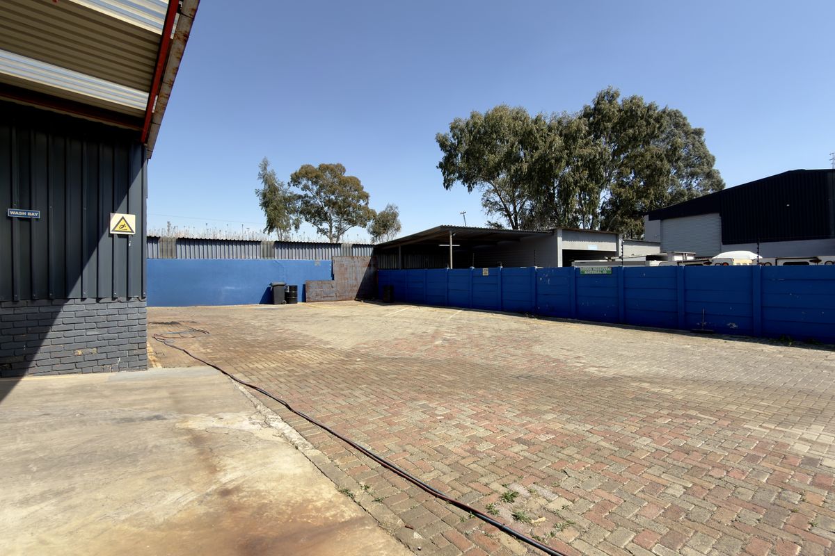 A spacious commercial paved yard area featuring a designated wash bay, enclosed by perimeter walls and adjacent to industrial metal-clad structures.